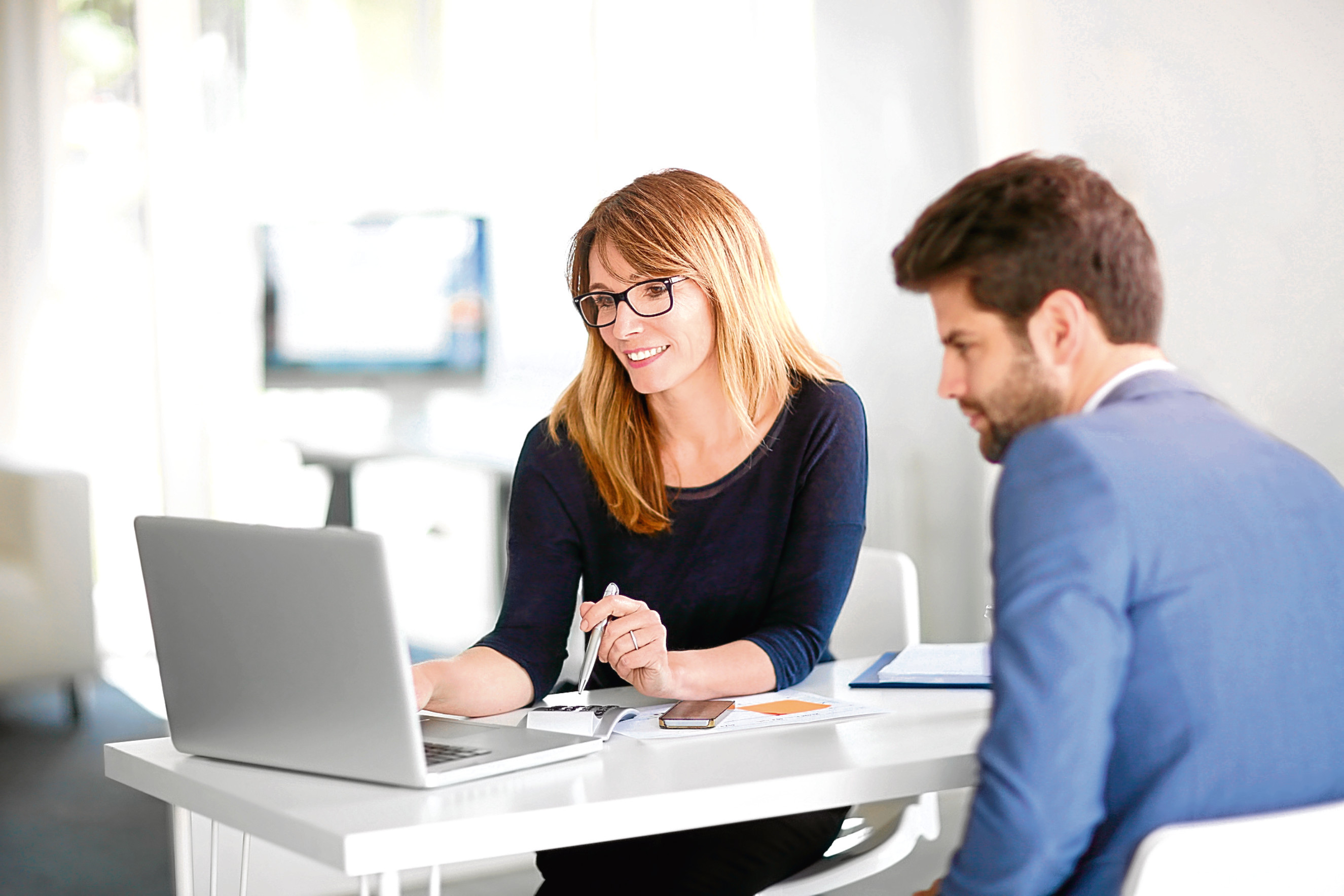 Portrait of investment advisor businesswoman sitting at office in front of computer and consulting with young professional man.