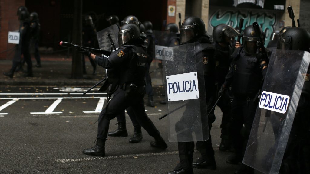 A Spanish National Police officer aims rubber-bullet rifle at pro-referendum supporters (Manu Fernandez/AP)