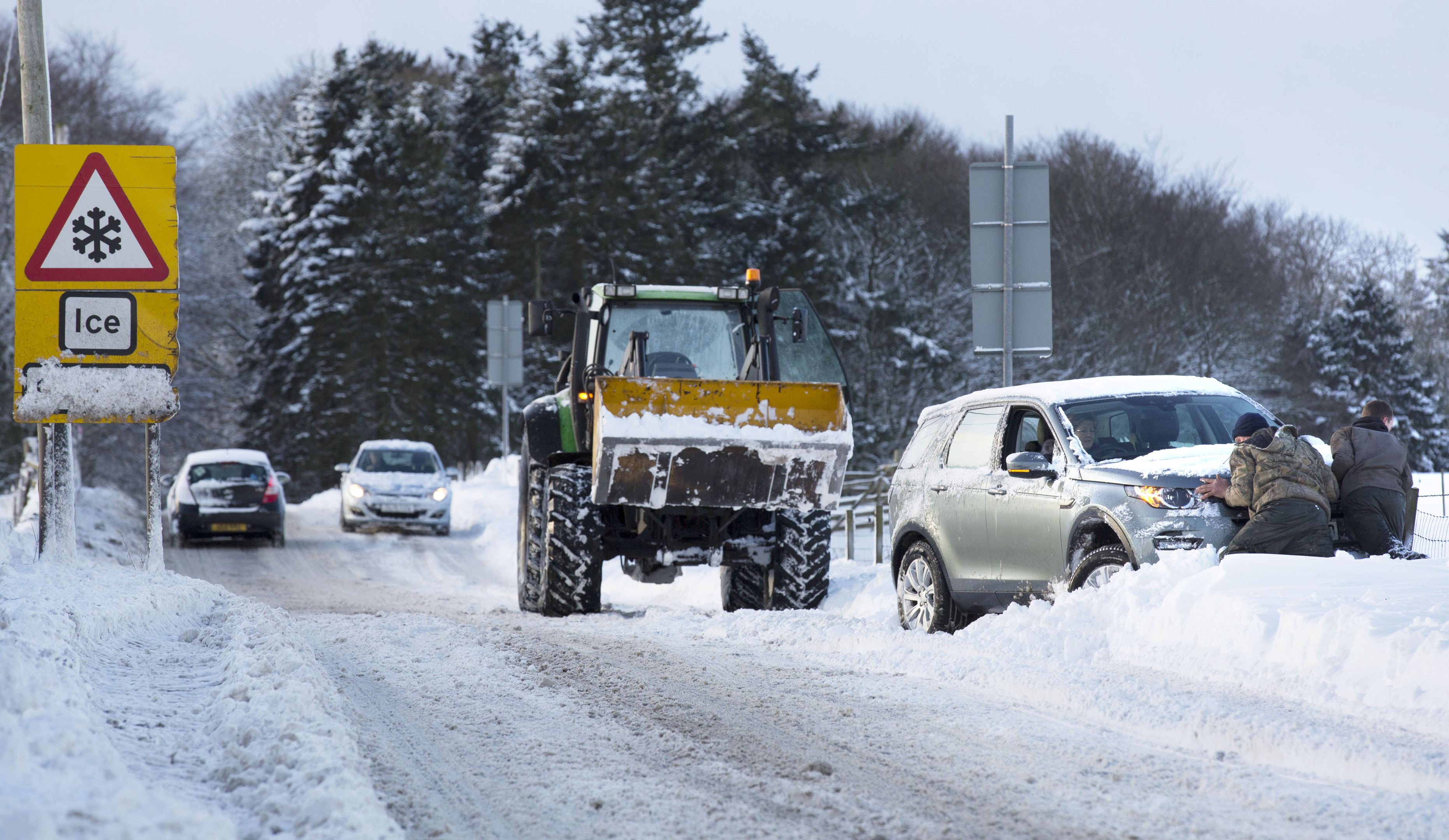 Drivers help to push a vehicle back on the road after heavy snow made road conditions difficult in Midlothian (David Cheskin/PA Wire)