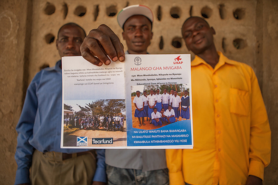 Village chiefs in Malawi hold up a leaflet carrying                         Tearfund and Scottish Government logos as part of work to eradicate child marriages (Chris Hoskins / TearFund)