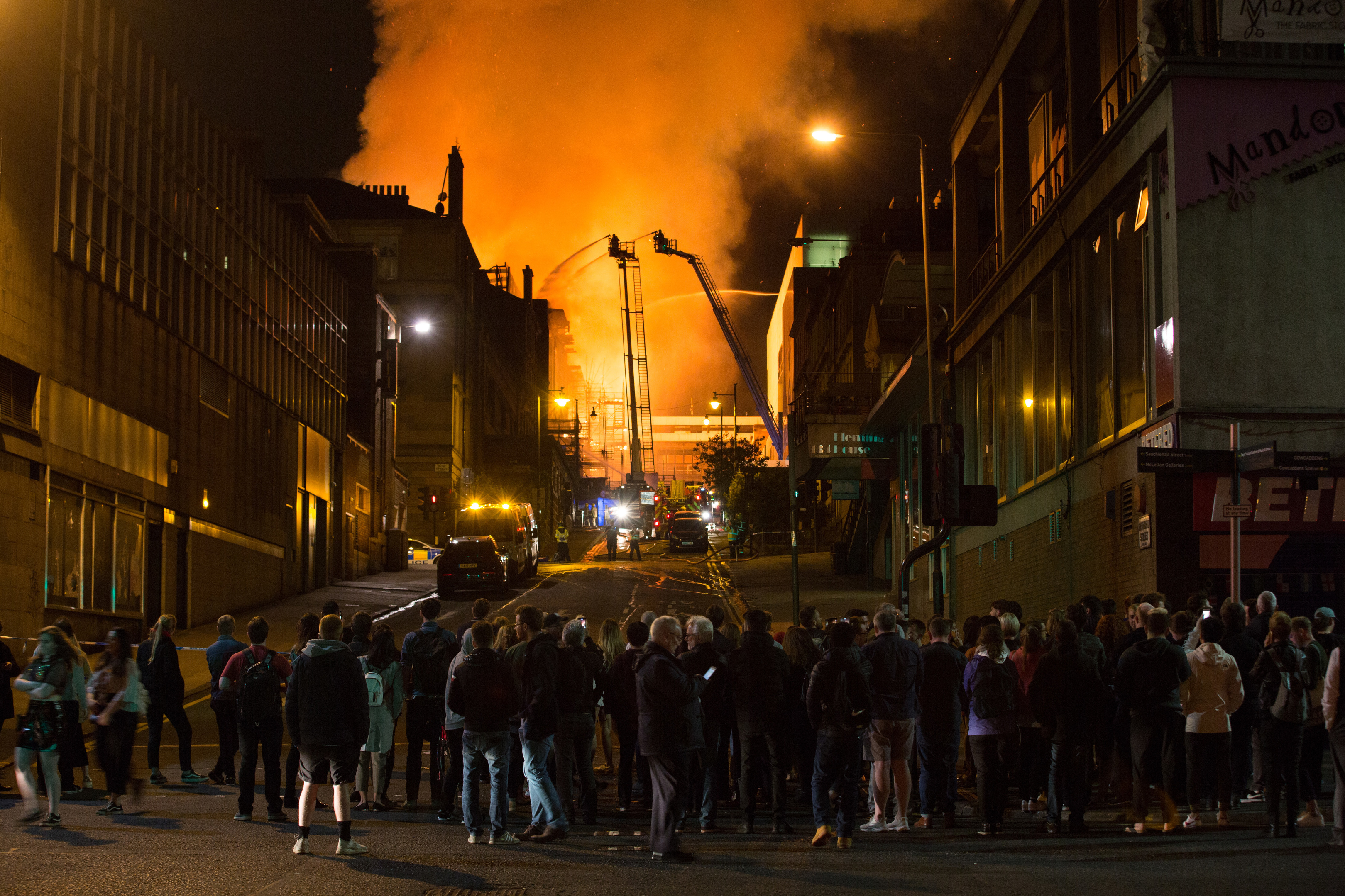 Onlookers huddle to watch the fire crews at work as fire engulfs the art school while the sky over Glasgow city centre glows from the flames just over a week ago (Robert Perry/Getty Images)