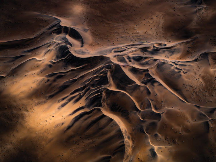 Tom Putt (Australia) Namib Desert, Namibia Flying low over the endless sand dunes of the Namib Desert, I noticed the cloud cover provided this interesting play of light on the landscape. When the sun heats up the dunes, it draws the black minerals to the surface. When I came to process the image, the stunning colours revealed themselves.