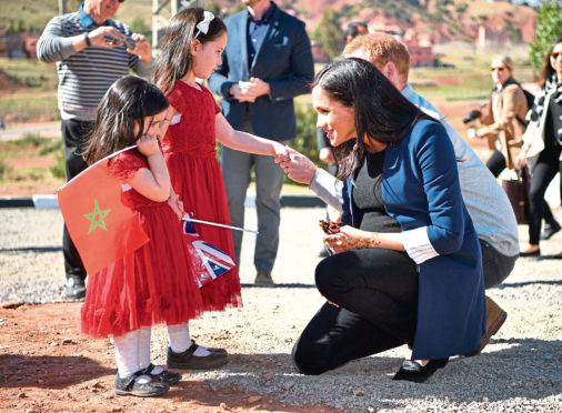 The Duke and Duchess of Sussex talk to two girls the henna design on her hand after a visit to the 'Education For All' boarding house in Asni Town, Atlas Mountains on the second day of her tour of Morocco with the Duke of Sussex.