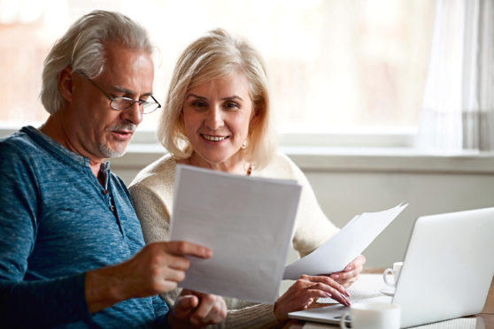 Happy old middle aged couple holding reading good news in document, smiling senior mature family excited by mail letter, checking paying domestic bills online on laptop, discussing budget planning