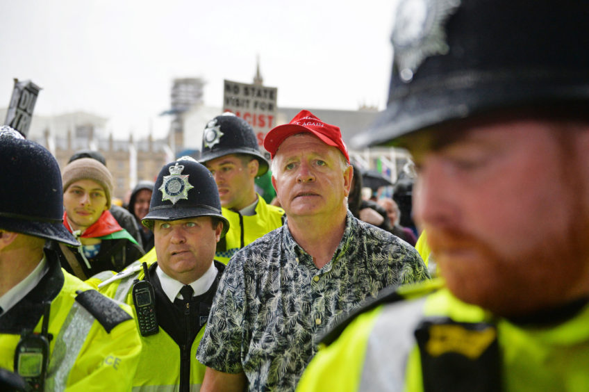 A Trump supporter is escorted by police after  being covered in milkshake at Parliament Square