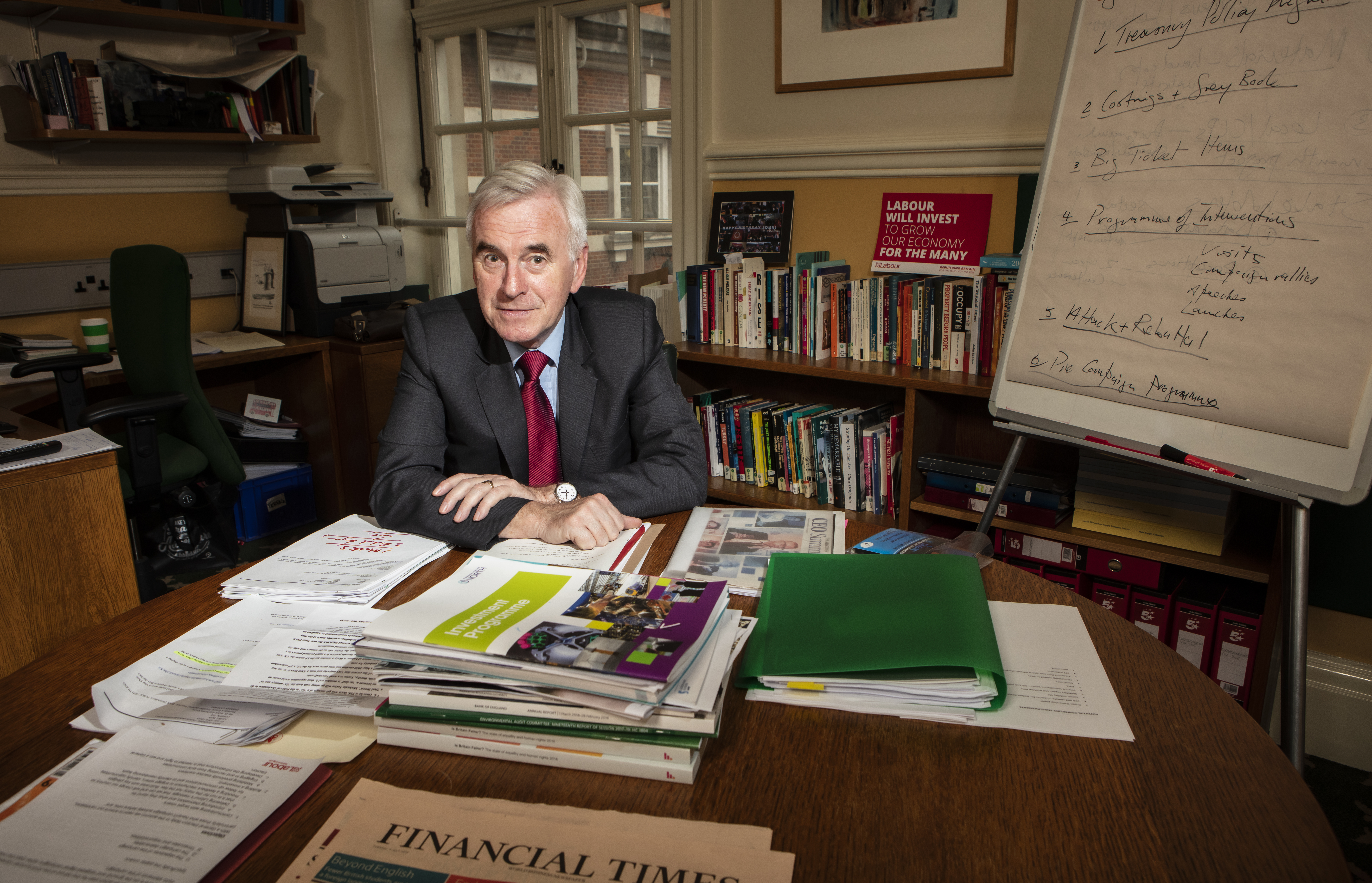 Shadow chancellor John McDonnell in his Westminster office and, behind him, the flipchart detailing Labour’s route to government