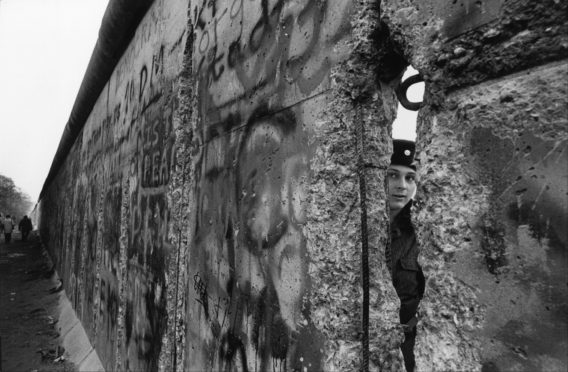 An East German soldier looks through the Berlin Wall in 1989