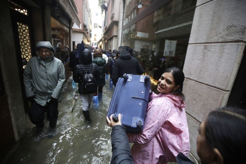 Tourists carry their luggage as they wade through water