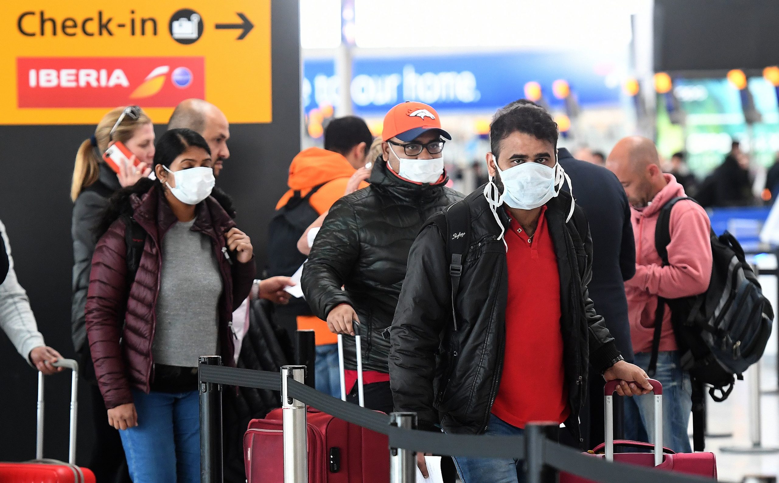 Travellers in masks queue at Heathrow airport in London as air travel grinds to a halt and nations                  across the world lock down their borders due to the coronavirus pandemic