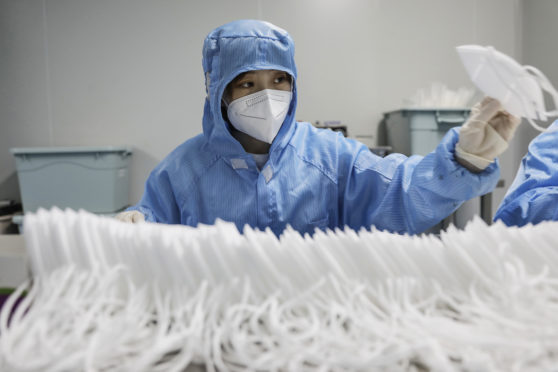 A worker wearing a protective suit and a face mask produces masks at a factory in China but unscrupulous traders are accused of charging customers rip-off prices