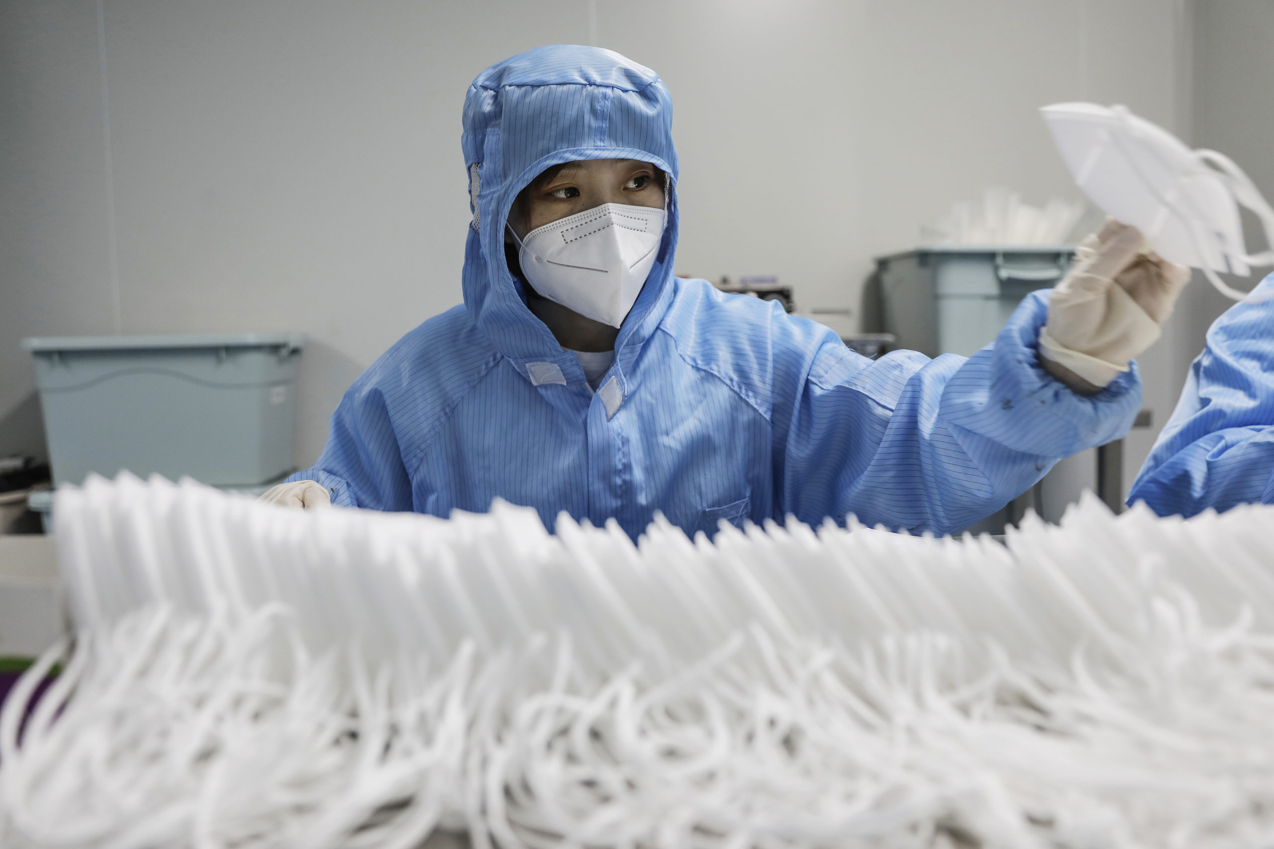 A worker wearing a protective suit and a face mask produces masks at a factory in China
