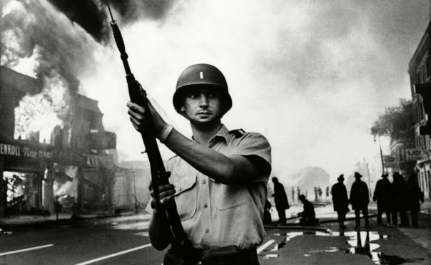 A Michigan national guardsman stands at the ready as firemen battle a blaze in a riot-torn district of Detroit in July 1967