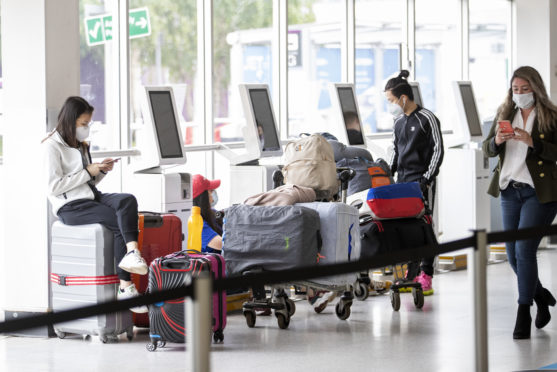 Passengers wearing protective face masks wait at the check-in area of Edinburgh Airport