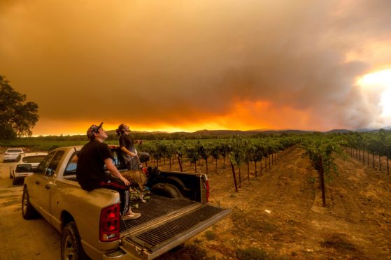 Locals watch as a plume of red smoke from the wildfires rises in the sky above Healdsburg, California