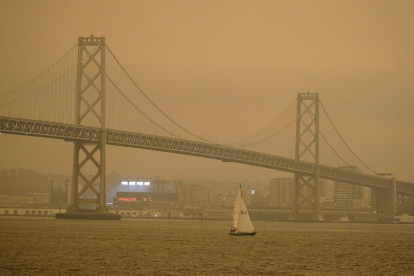 Under darkened skies from wildfire smoke, a sailboat makes its way past the San Francisco-Oakland Bay Bridge