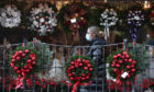 A person wearing a face covering walks passed Christmas wreaths for sale at All Occasions Designer florist in Denny