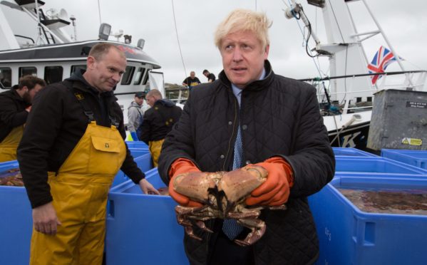 Prime Minister Boris Johnson holds a crab caught on the Carvela with Karl Adamson at Stromness Harbour in Stromness during a visit to the Highlands and Northern Isles of Scotland.