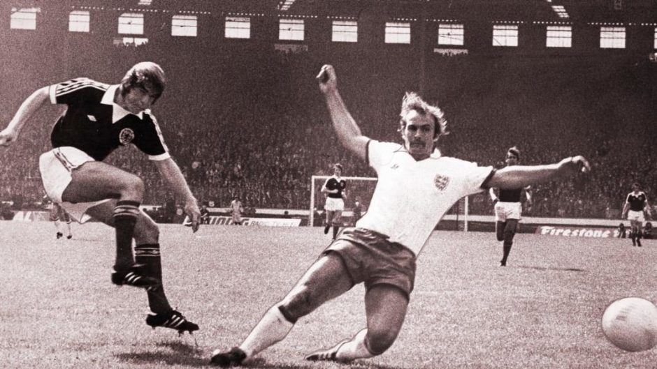 Kenny Dalgish scoring against England in 1976. The ball bobbles along the turf and then goes through Clemence's hands and then his legs.