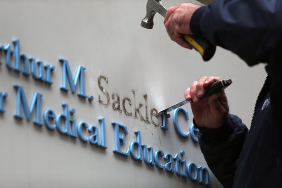 A Tufts University employee removes letters from signage featuring the Sackler family name at the Tufts building in Boston in December 2019