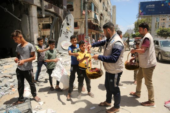 Aid workers hand out fruit and sweets to Palestinian children amid the rubble of Gaza City following days of Israeli air strikes