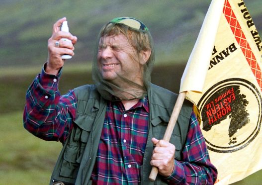 A man wearing a net sprays midge repellent in the Highlands