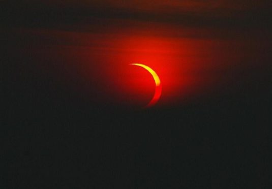 The cloud cover moves for just a moment to display the moon passing in front of the sun at the end of its phase on the cliff tops near Durness in Sutherland, North of Scotland.