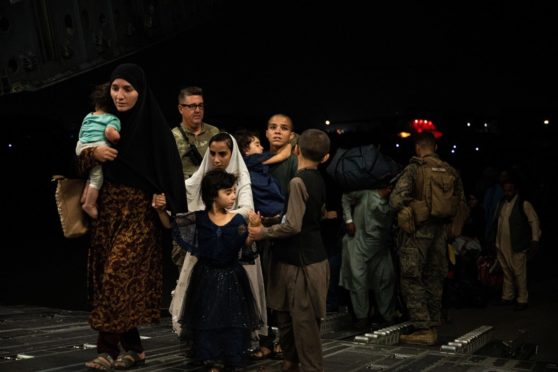 An Afghan family, carrying a few possessions and young children, board a military plane full of refugees, above and below, at Kabul airport yesterday