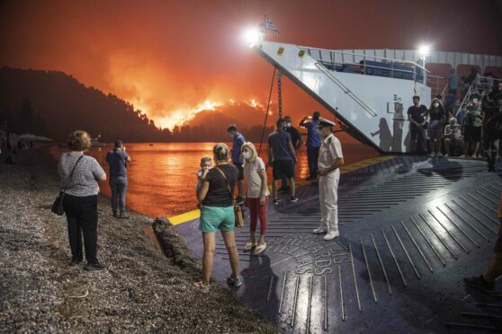 People board a ferry prior to an evacuation as a wildfire approaches the seaside village of Limni, on the island of Evia, Greece.