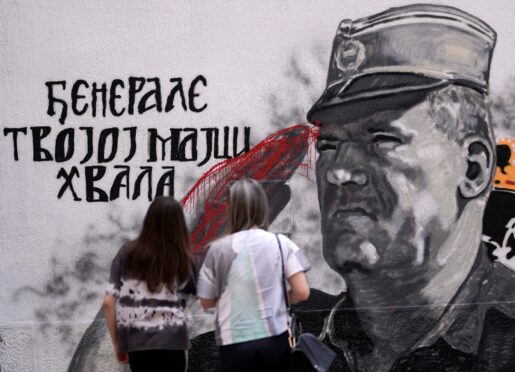 Two women in front of a mural of former Bosnian Serb military chief and convicted war criminal Ratko Mladic that has been vandalised with paint in Belgrade