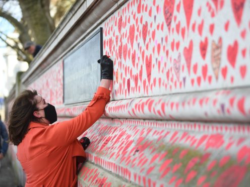 A woman takes part in the final stages of painting approximately 150,000 hearts on to the National Covid Memorial Wall on the Embankment in London (Victoria Jones/PA)