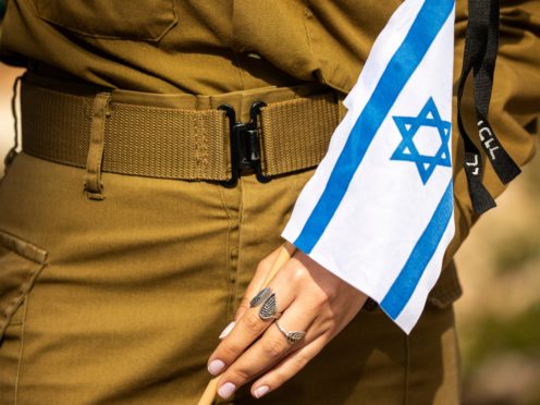 An Israeli soldier holds a flag with black ribbon attached to it as she stands by an Israeli soldier’s grave ahead of the country’s memorial day for fallen soldiers and victims of attacks, at the Kiryat Shaul Military Cemetery in Tel Aviv, Israel, Tuesday, April 13, 2021. Memorial Day begins at dusk on Tuesday and lasts until Wednesday evening. (AP Photo/Ariel Schalit)