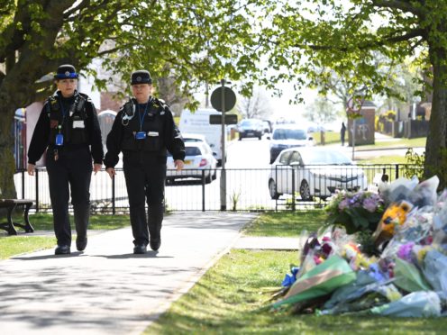 Police Community Support Officers walk past floral tributes in a park in Aylesham village (PA)