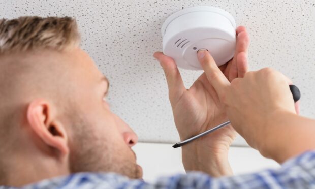 A man fixing a fire alarm in preparation of the new interlinked smoke alarms Scotland legislation