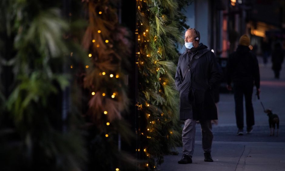 A man wearing a face mask passes an illuminated Christmas window display outside a shop during the coronavirus pandemic.