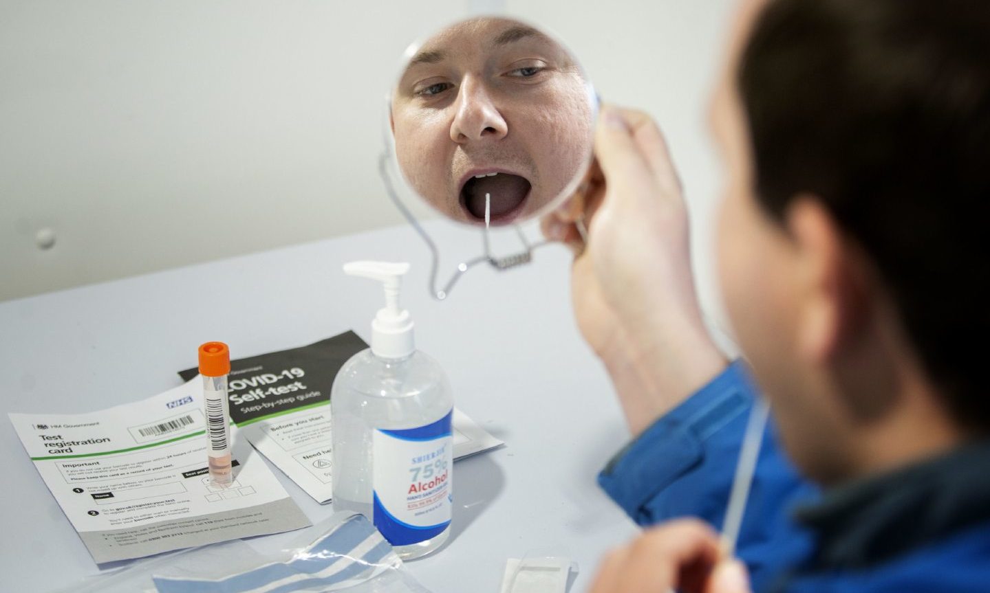 A man self-administering a rapid covid test in the mirror
