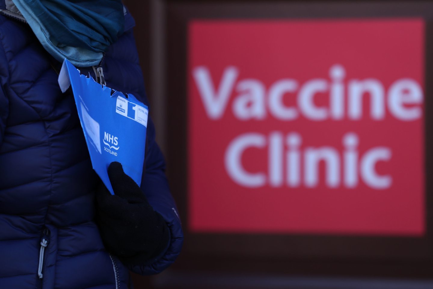 Someone leaves a vaccination centre while holding their blue appointment letter.