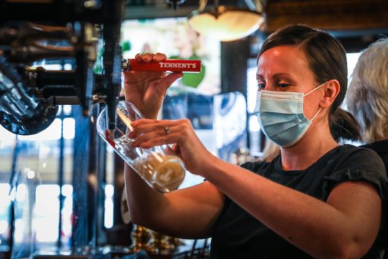A woman in a mask pouring a pint of beer in a Scottish restaurant