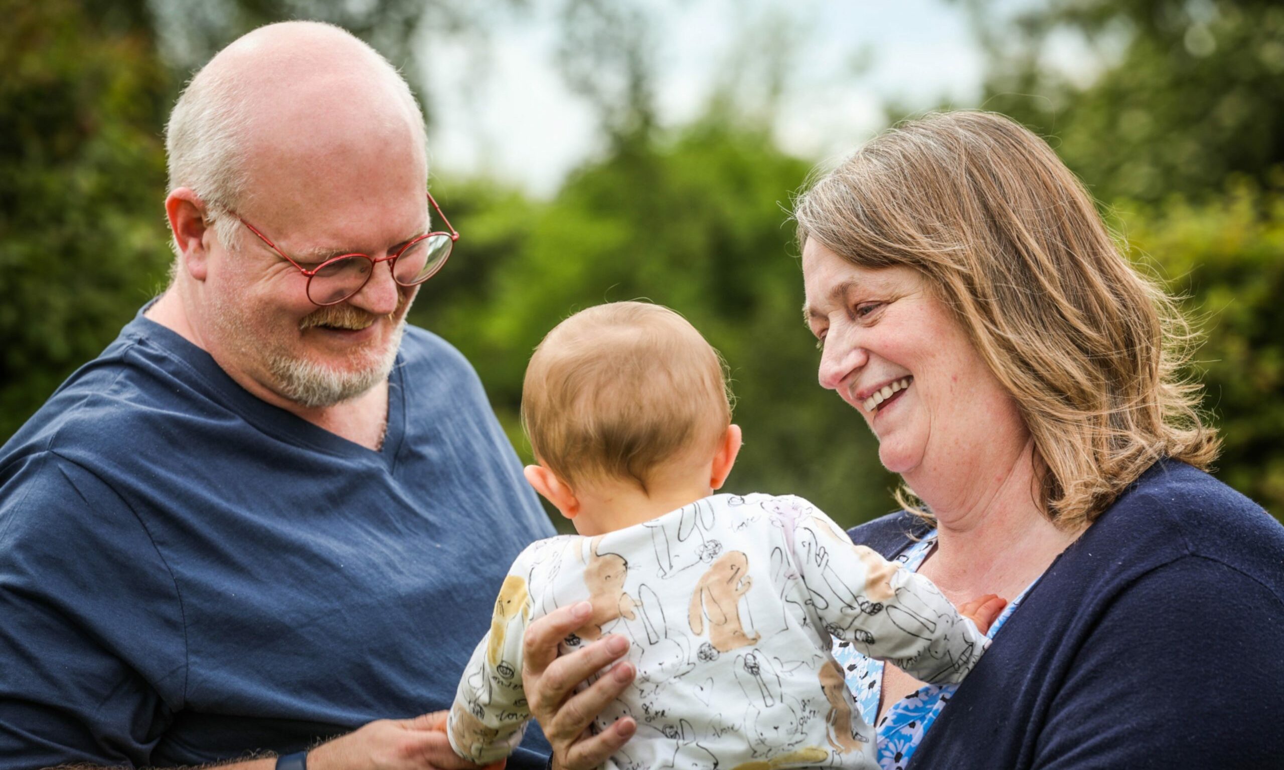 Two foster carers, a man and a woman, holding a baby and smiling