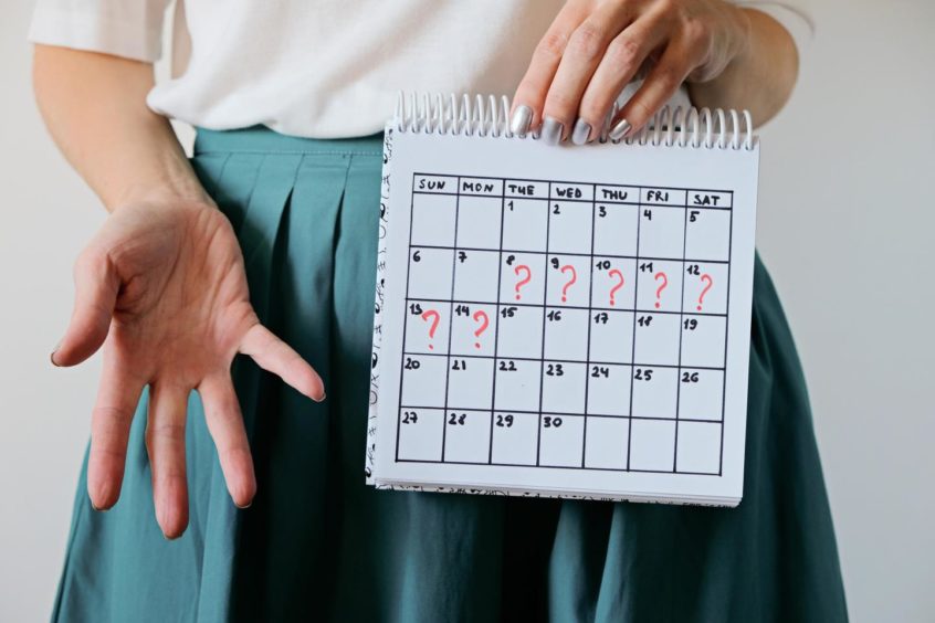 A woman holding a calendar with question marks written in each day. 