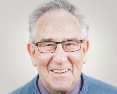 A close up shot of Rev Ken Gordon pictured in his later years. His hair is greying and he's wearing black thin-rimmed glasses with a wide smile. 