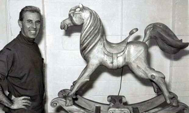 Black and white image of Iain McIntosh standing to the left of a wooden rocking horse he made for Harrods department store