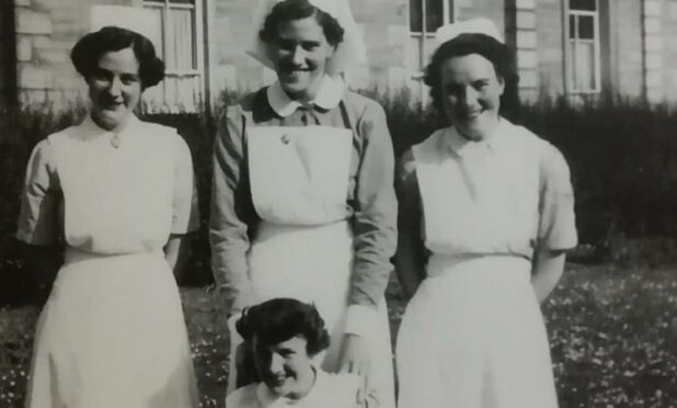 black and white image of trainee nurses pictured outside hospital building, wearing white nurses' hats and aprons. Evelyn MacKenzie is shown sitting front and centre of the image