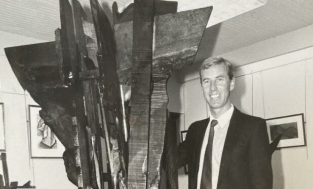 Black and white image of Iain McIntosh beside a huge, jagged wooden sculpture that towers over him.