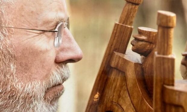 A spectacle-wearing Iain McIntosh looks closely at a wooden sculpture he has made