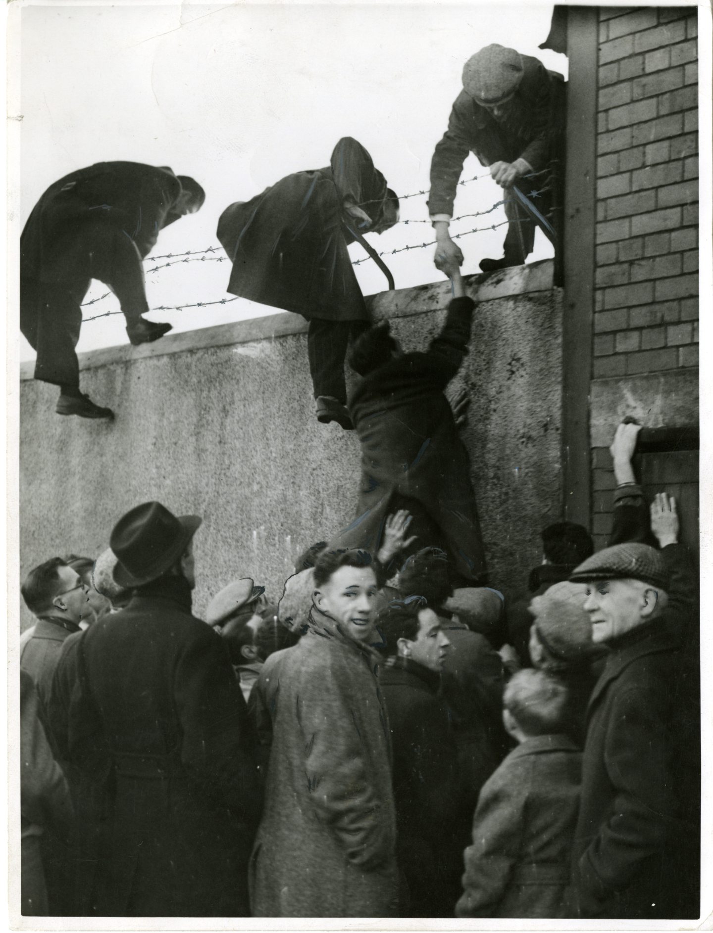 Fans scale the walls at Dens Park so they can watch the game taking place between Dundee and Rangers in January 1949.