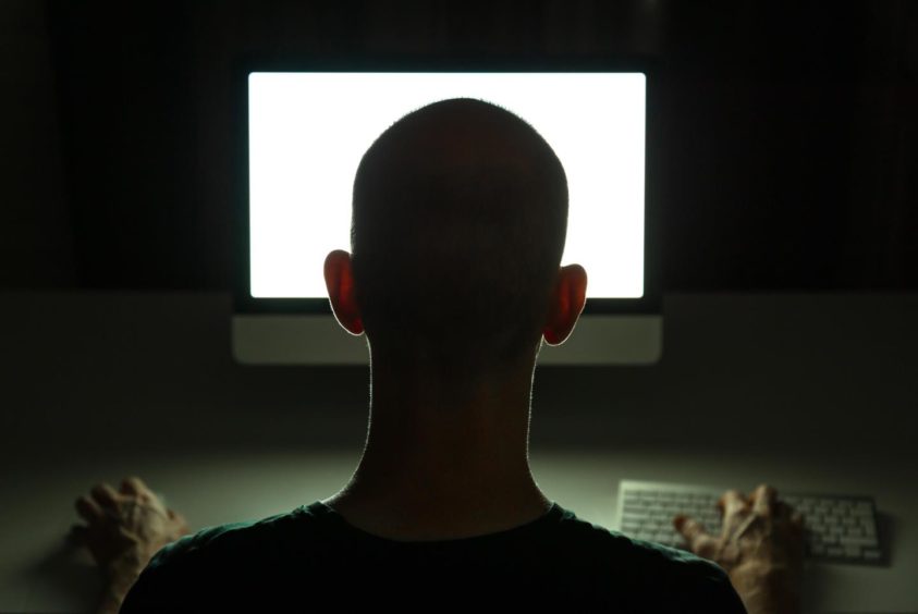 A man looking at a desktop computer screen in the dark.