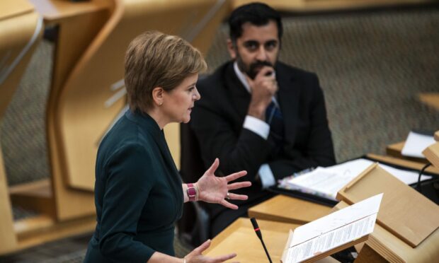 Nicola Sturgeon talking in parliament with Humza Yousaf looking on