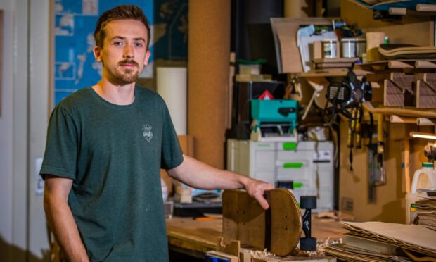 Malcolm Bradley at his work desk holding a small wood and cork skateboard.