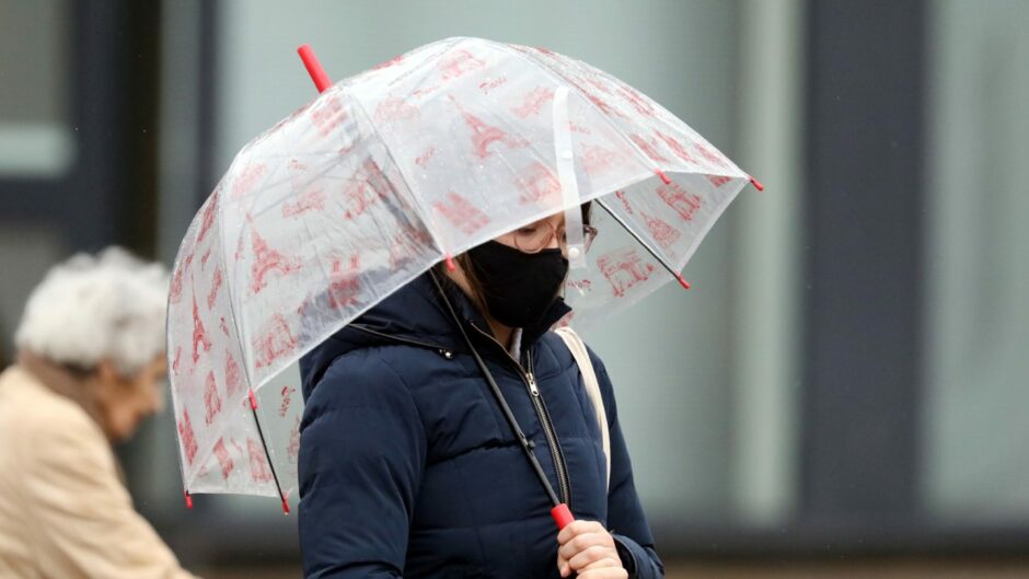 A person walking under an umbrella in Dundee city centre during heavy rain.