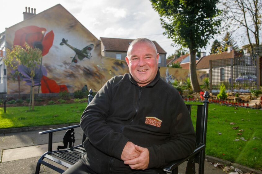 Community champion Bob McPhail sits beside a new mural at the war memorial.